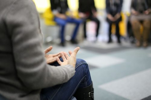 A woman having a group therapy session around other patients.
